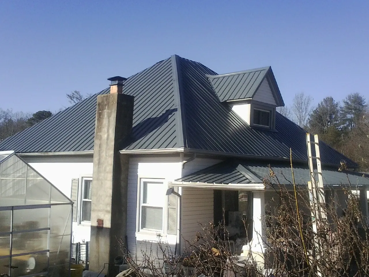 Dark blue standing seam metal roof on a white farmhouse with dormer — Slate & Tile Roof Repair by Roofing Brothers in Stirum