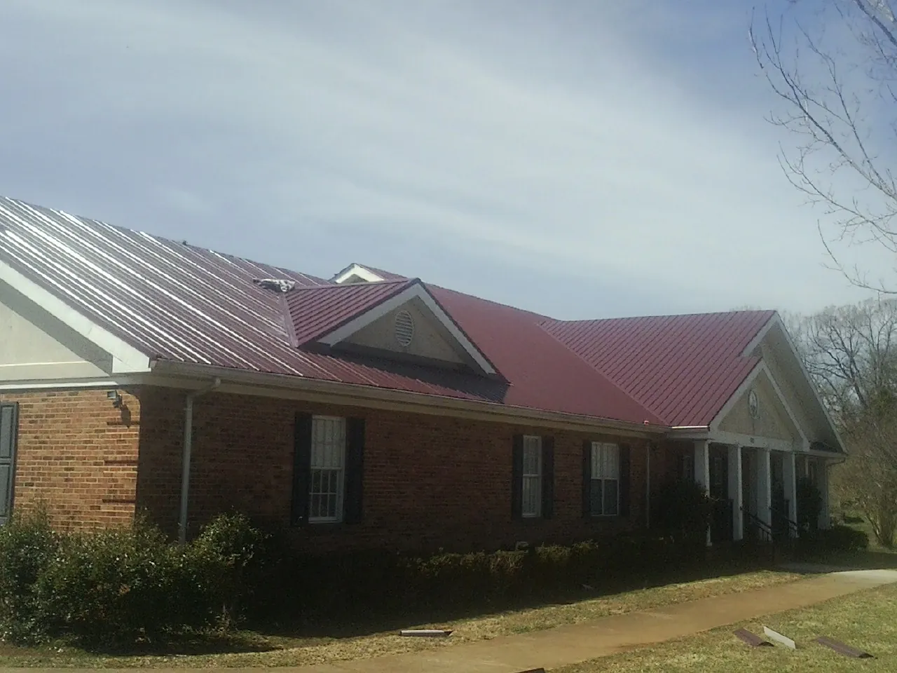 Red metal roof with gabled entries on a long brick building, from a Hail Damage Roof Repair job in Stirum