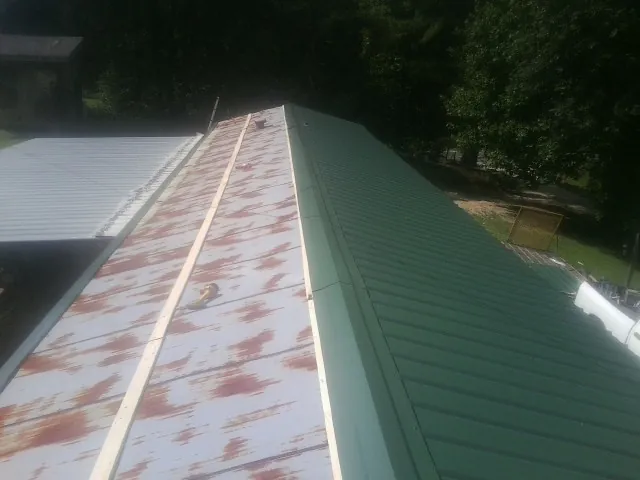 Old rusted panels beside newly installed green metal roofing — Wind Damage Roof Repair by Roofing Brothers in Stirum