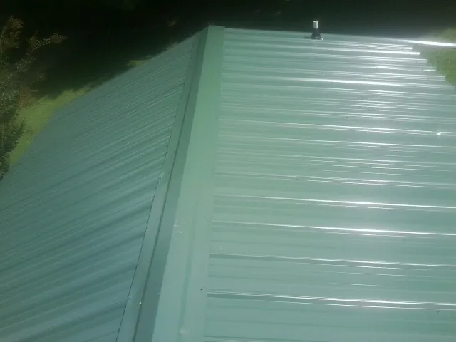 New green metal panels meeting at the ridge of a roof — Flat Roof Repair work by our crew in Stirum