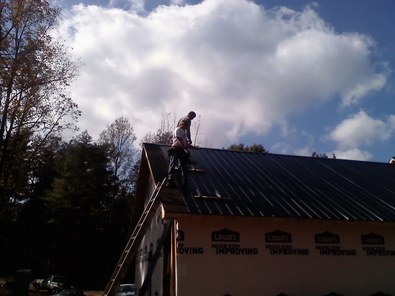 Roofer fastening dark metal panels high against a cloudy sky, from a Roof Inspection job in Stirum