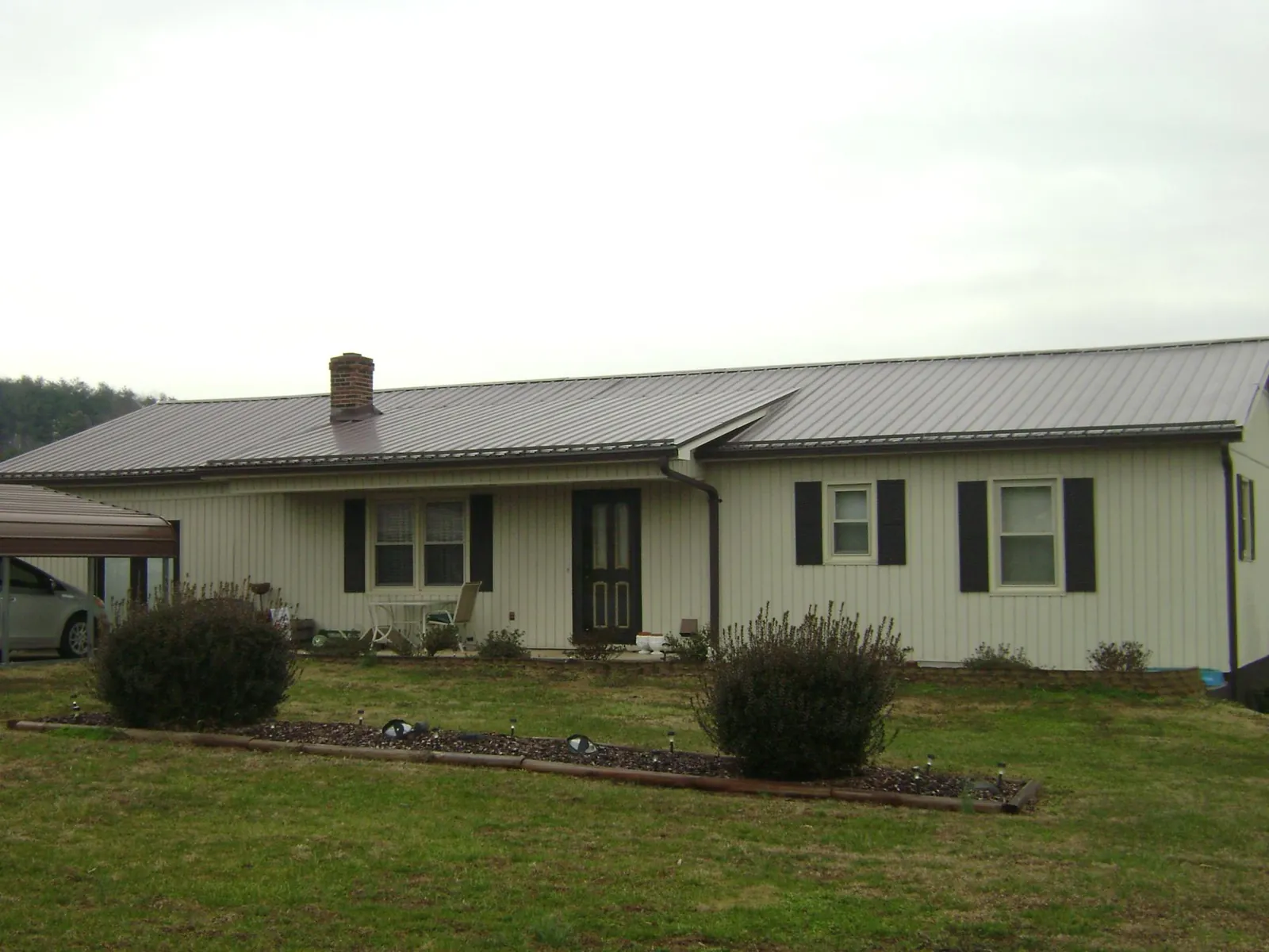 Brown metal roof on a cream sided ranch home with a brick chimney in Stirum