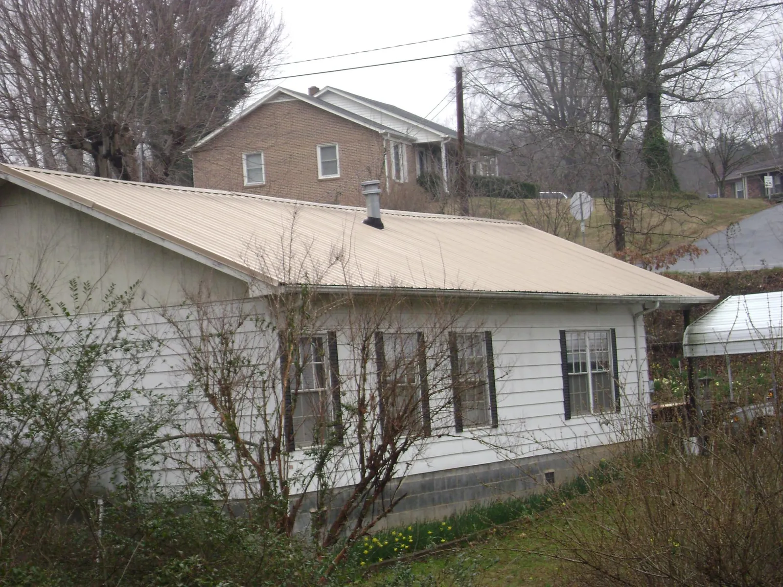 Tan metal roof on a white sided house set into a hillside — Commercial Roofing by Roofing Brothers in Stirum