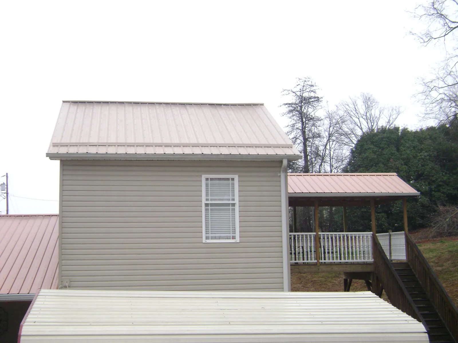 Tan metal roofs on a two story addition and attached porch, from a Roof Replacement job in Stirum